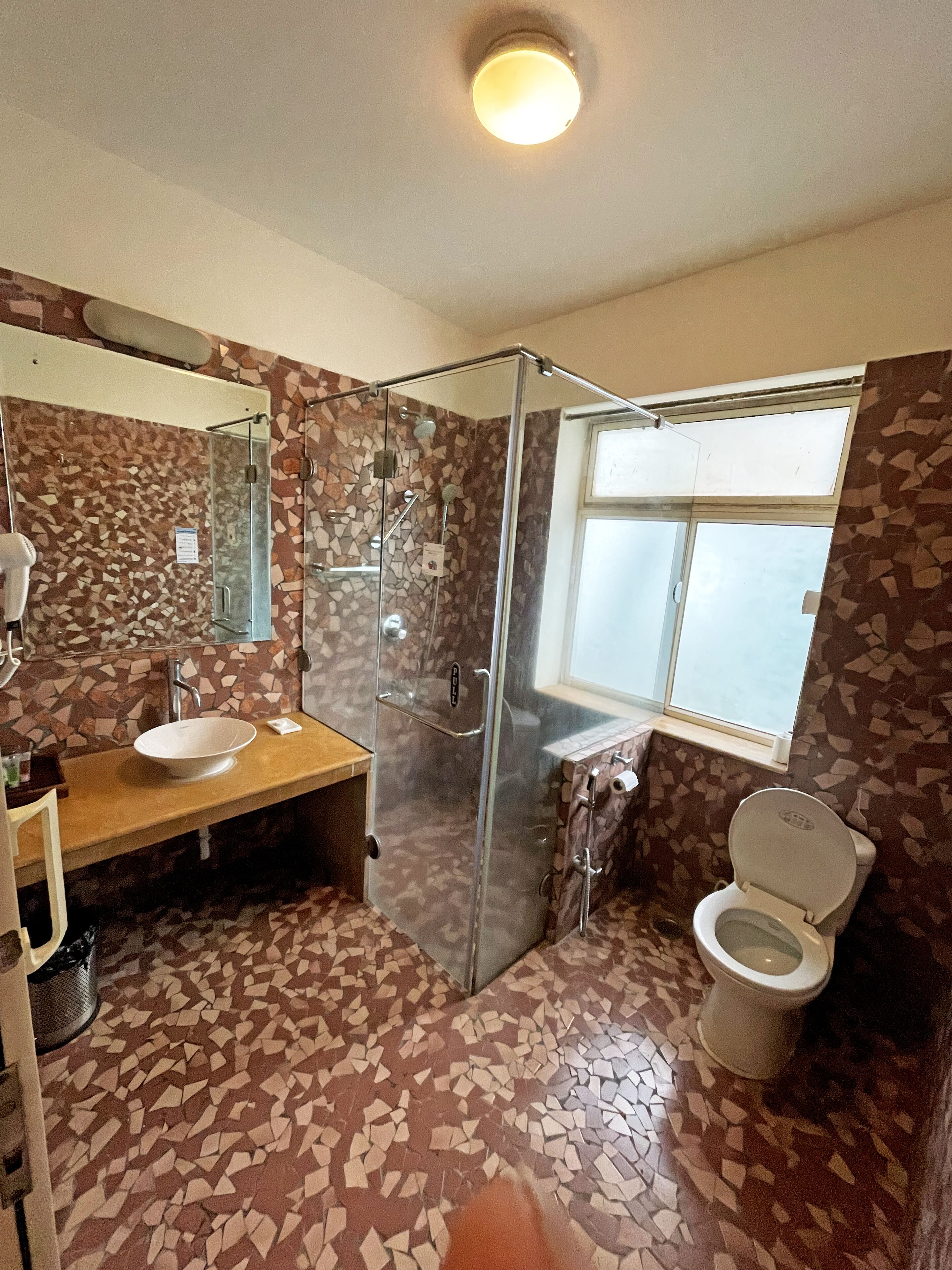 Un baño con piso de mosaico, cabina de ducha de vidrio, lavamanos con espejo e inodoro.