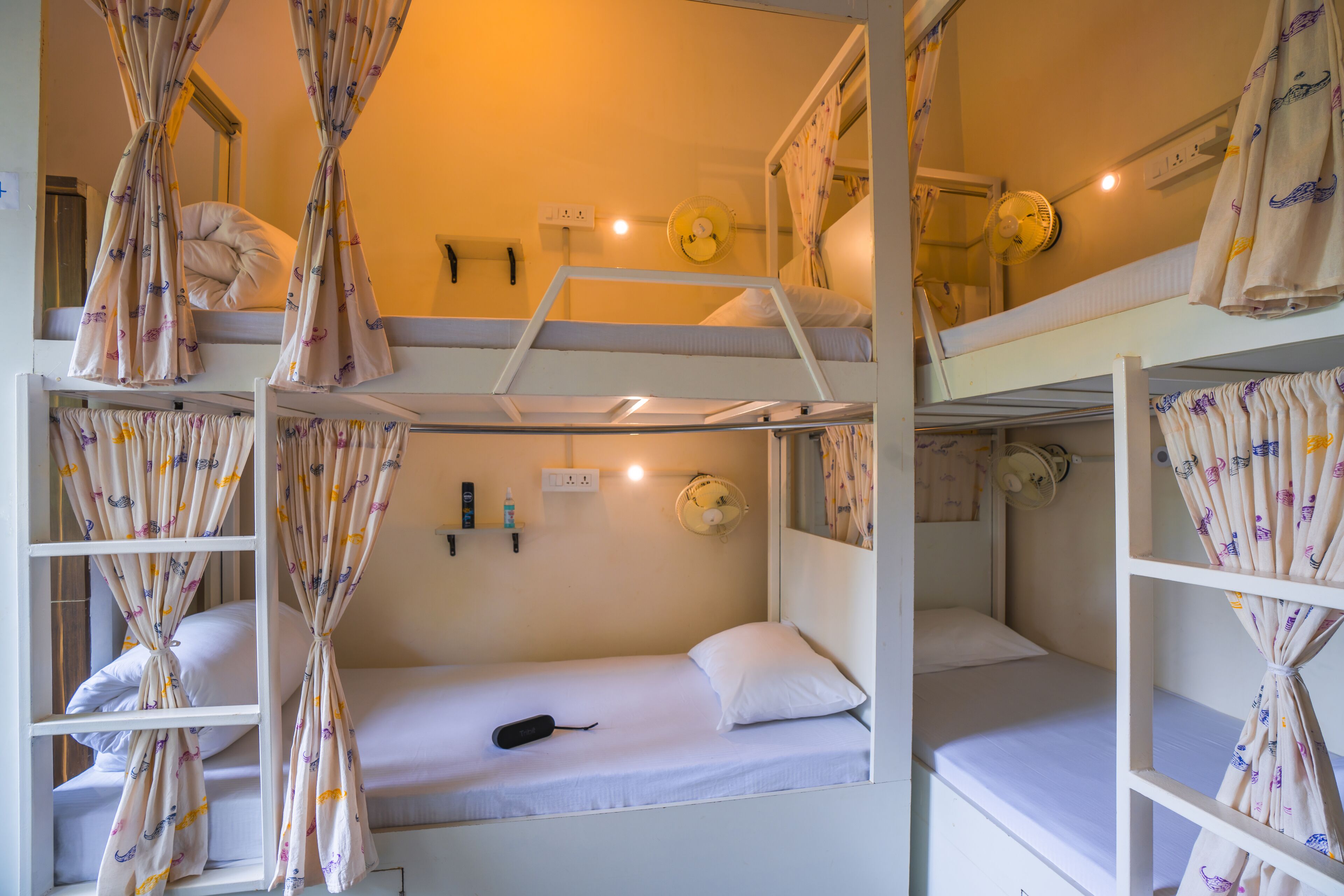 Een slaapkamer met stapelbedden, gordijnen, een ventilator en een spiegel.