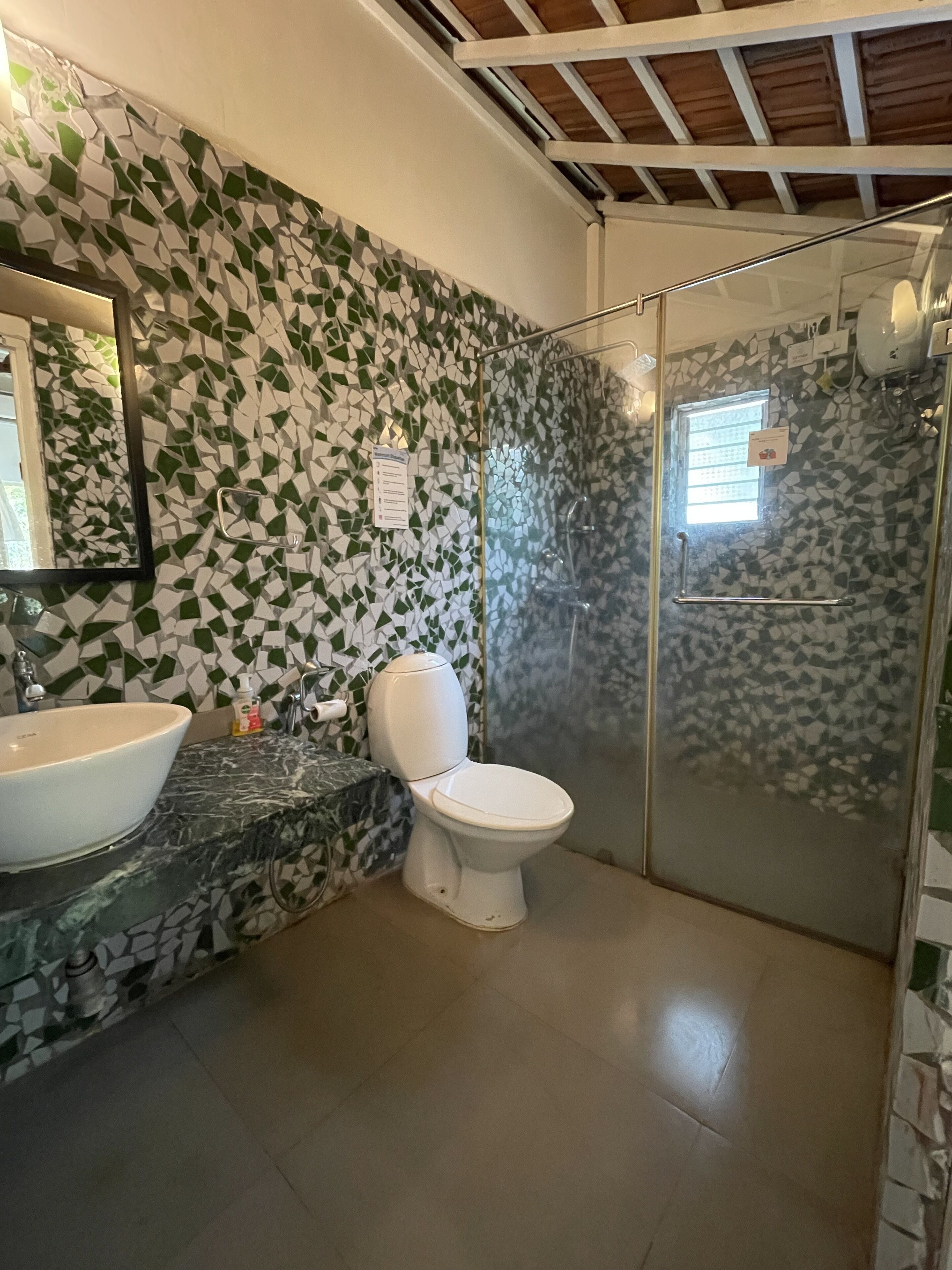 A bathroom with a mosaic wall, a white toilet, a sink, and a glass shower enclosure.