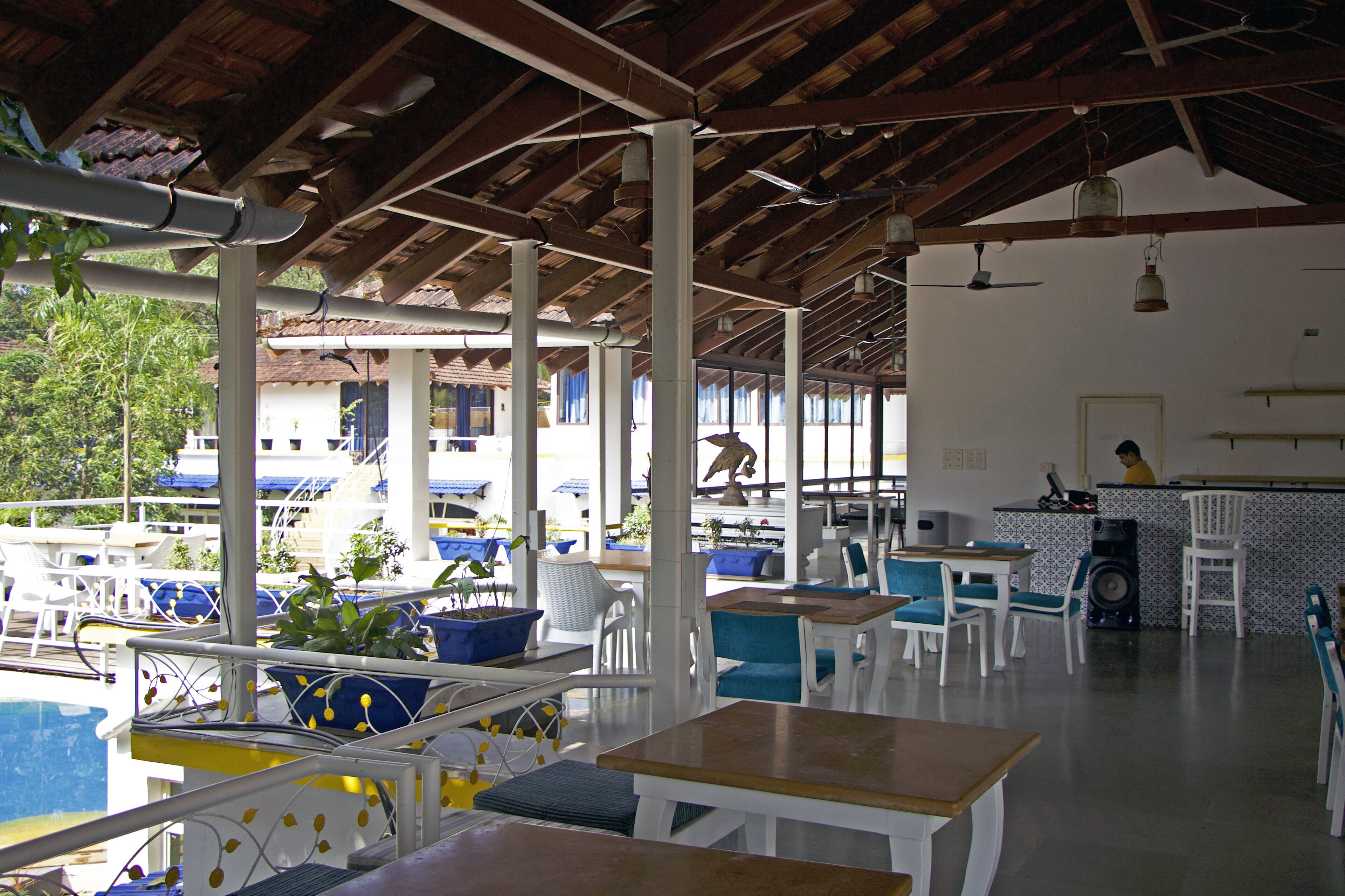 An outdoor seating area with white tables and chairs, surrounded by a pool and a building with a tiled roof.