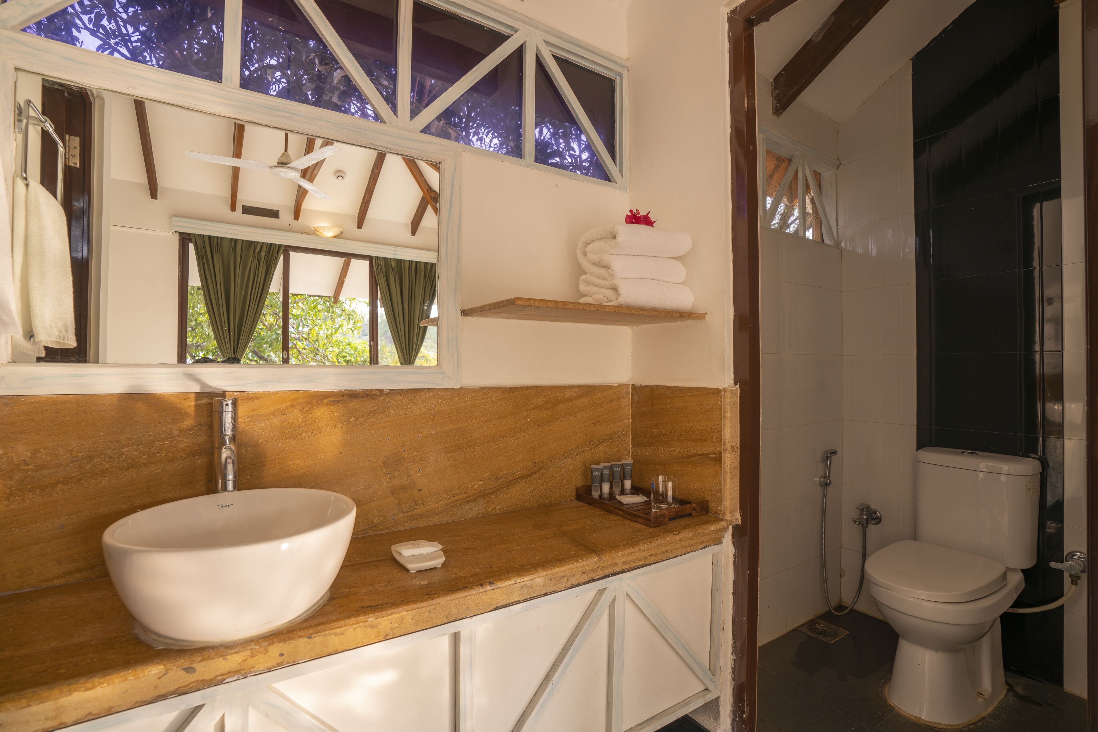 A bathroom with a wooden vanity, a white sink, a window with curtains, and a toilet.