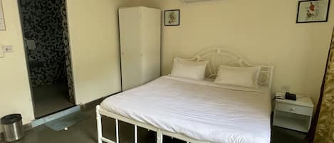 A bedroom with a single bed, a wardrobe, a small bedside table, and an air conditioning unit on the wall.