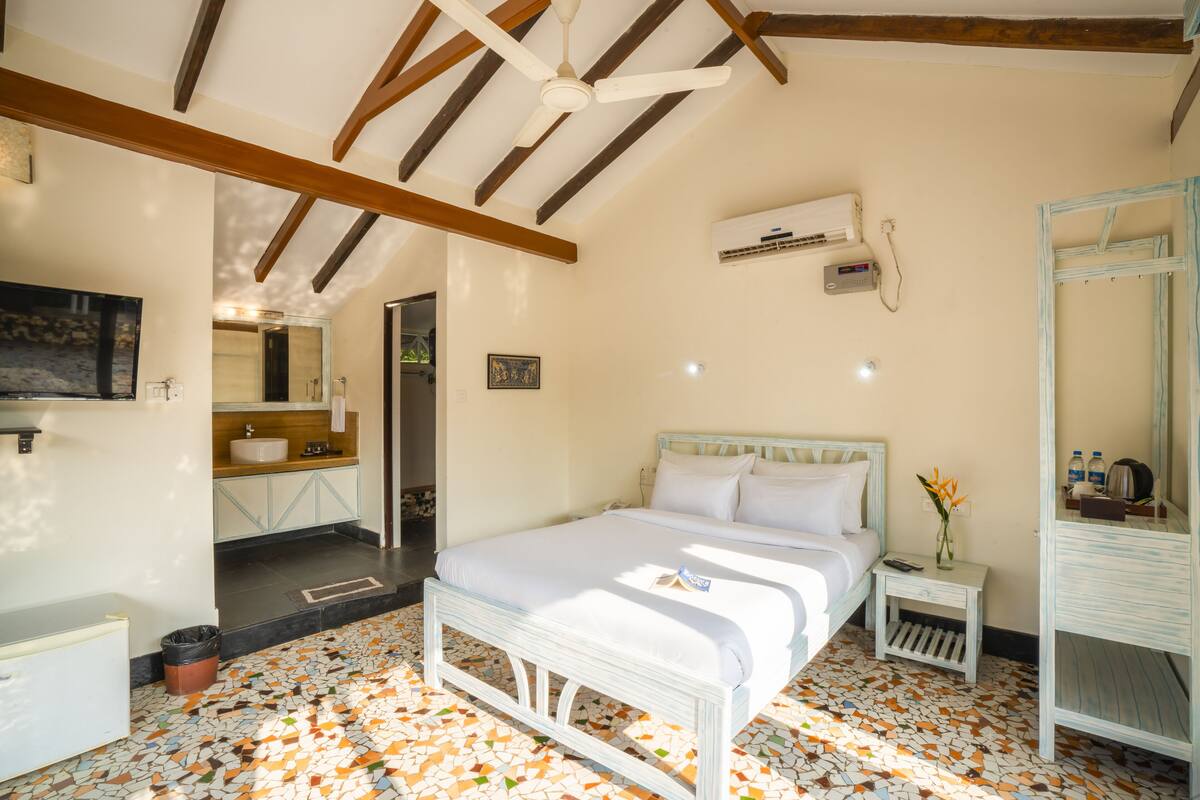 A bedroom with a white bed, a nightstand, a mirror, and a bathroom visible through an open door.