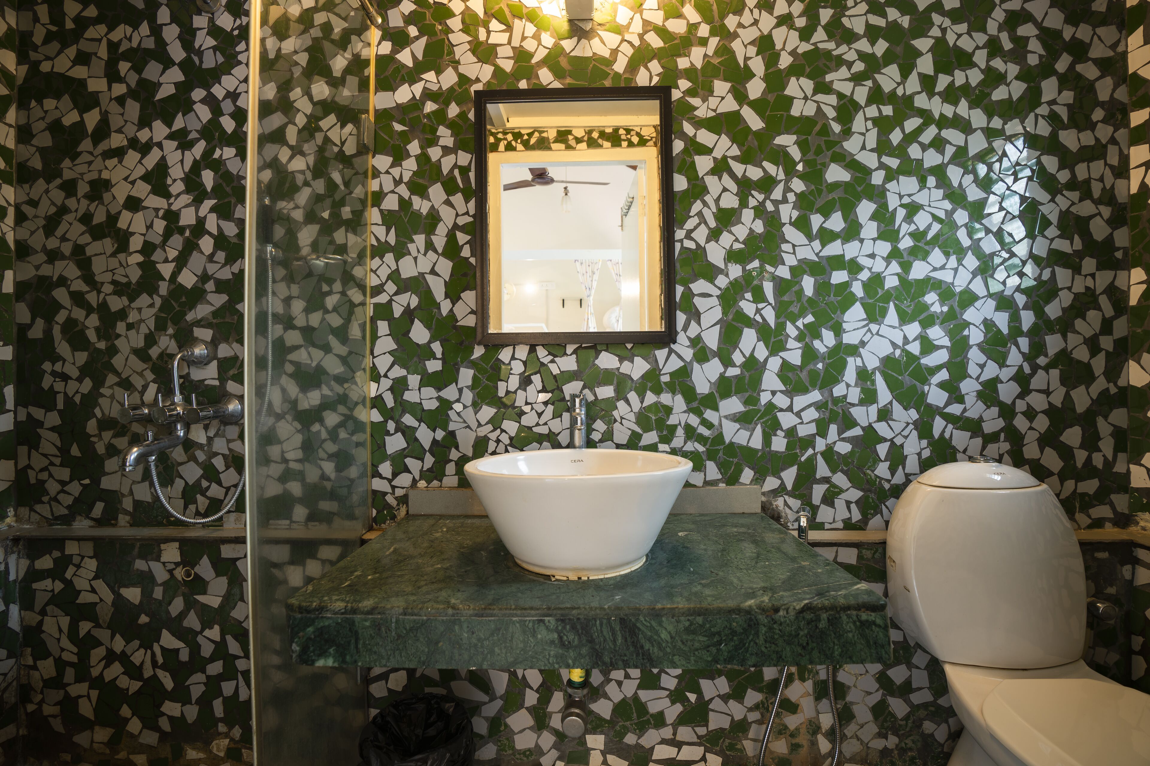 A bathroom with a mosaic tile wall, a white sink, a toilet, and a shower with a glass door.