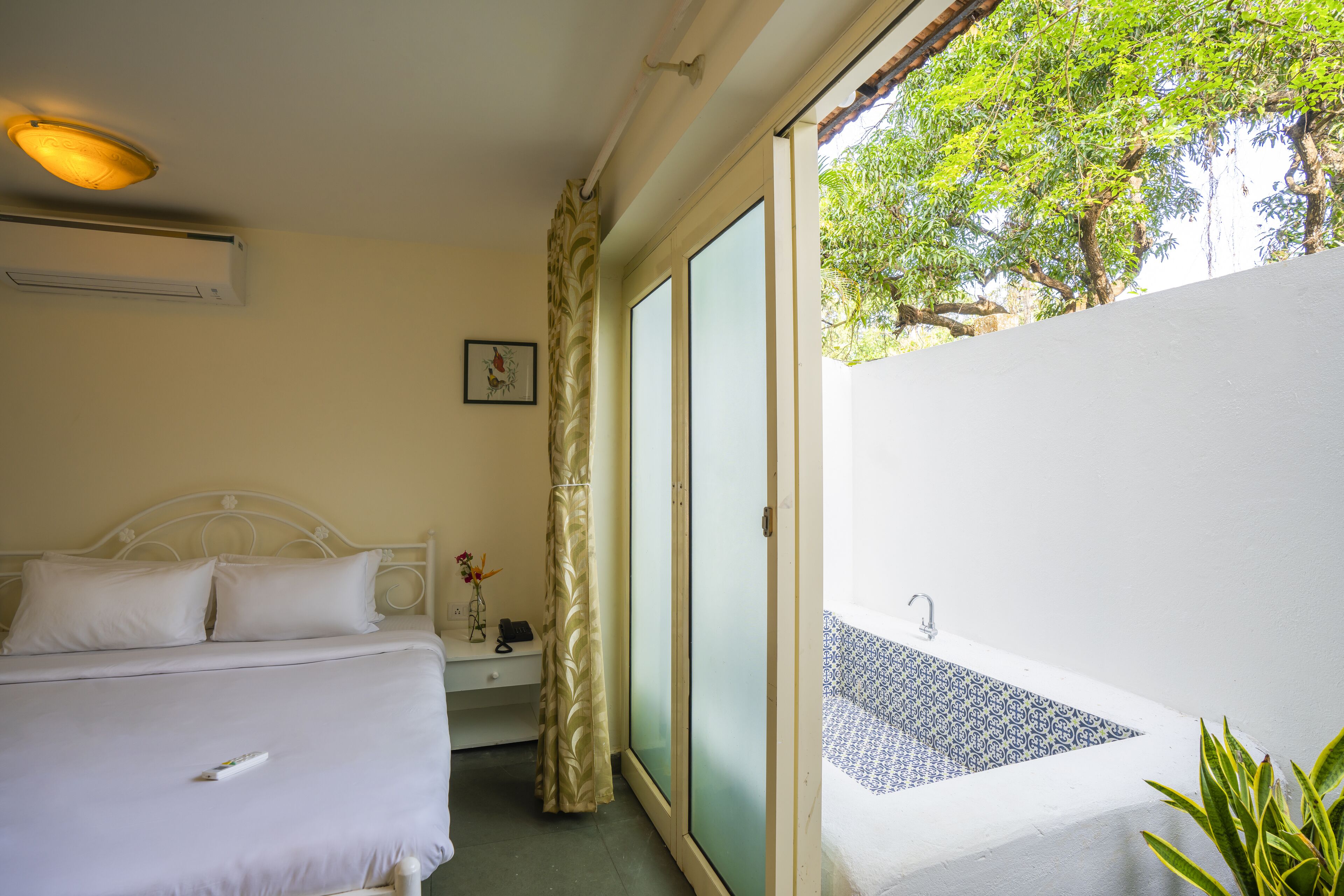 A bedroom with a bed, a nightstand, a window with a curtain, and a view of a pool.