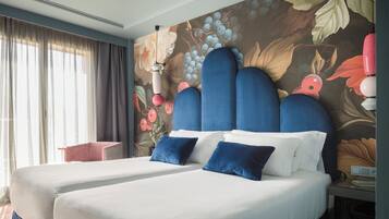 A hotel room with two beds, a large floral mural on the wall, and a window with sheer curtains.
