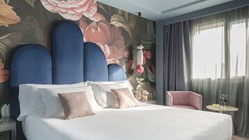 Una habitación de hotel moderna con una cama grande, una mesita auxiliar, una silla y un ventanal con cortinas.