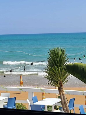 A beachside view with a palm tree, chairs, and tables, overlooking the ocean. - Natura Pura Wellness Oasis near Laghetti di Cavagrande (Avola)