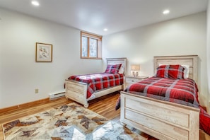 A bedroom with two beds, a rug, a window, and a wall-mounted picture.
