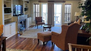 A spacious living room with hardwood flooring, a fireplace, a television, and a ceiling fan. - Beachside Breeze - Pools, hot tub, & private beach access (Kill Devil Hills)