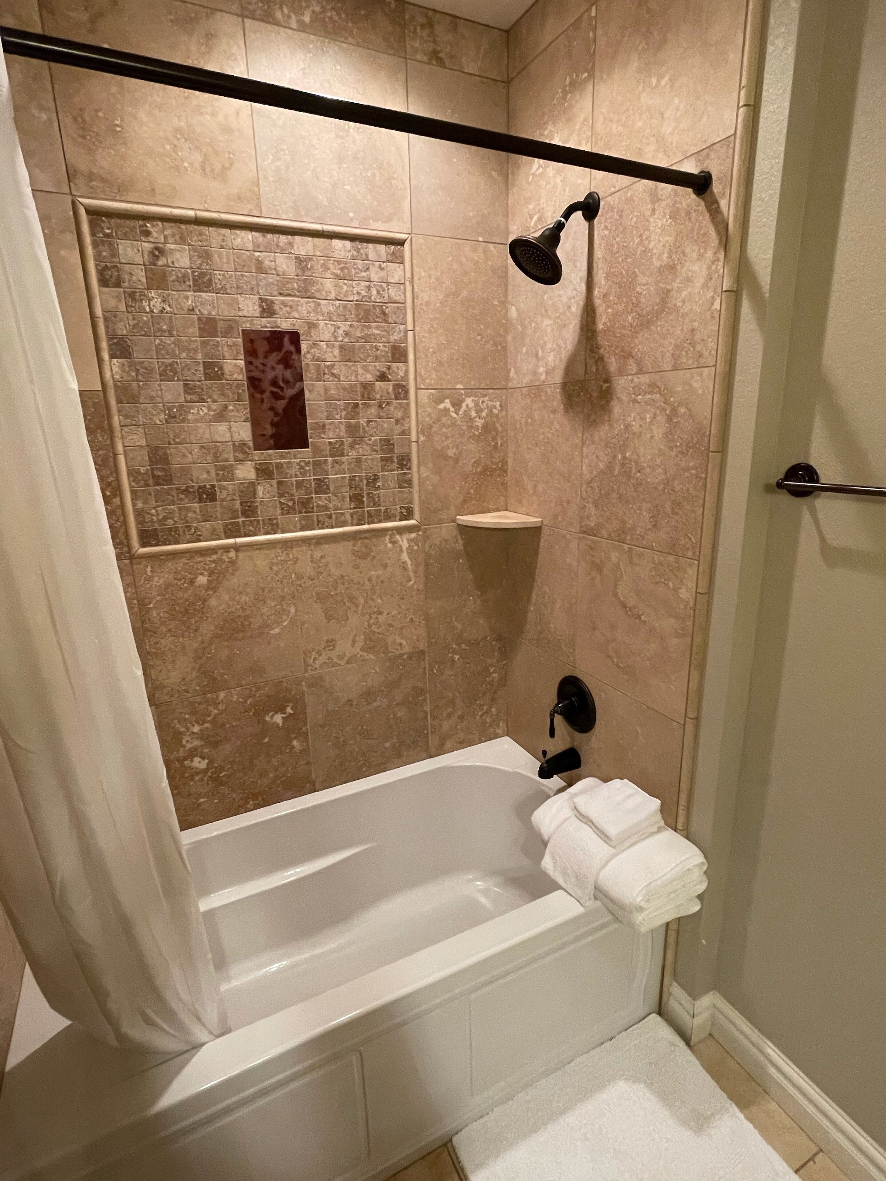Un baño con bañera, ducha y pared de azulejos.