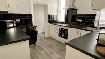 A modern kitchen with white cabinets, black countertops, and a grey herringbone floor.