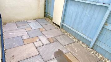 A patio with stone tiles and a blue wooden fence.