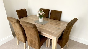 A wooden dining table with six brown upholstered chairs, a white vase with flowers, and a gray placemat. - Spacious Two Bed Apartment in Poole (Poole)