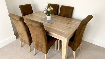 A wooden dining table with six brown upholstered chairs, a white vase with flowers, and a gray placemat.