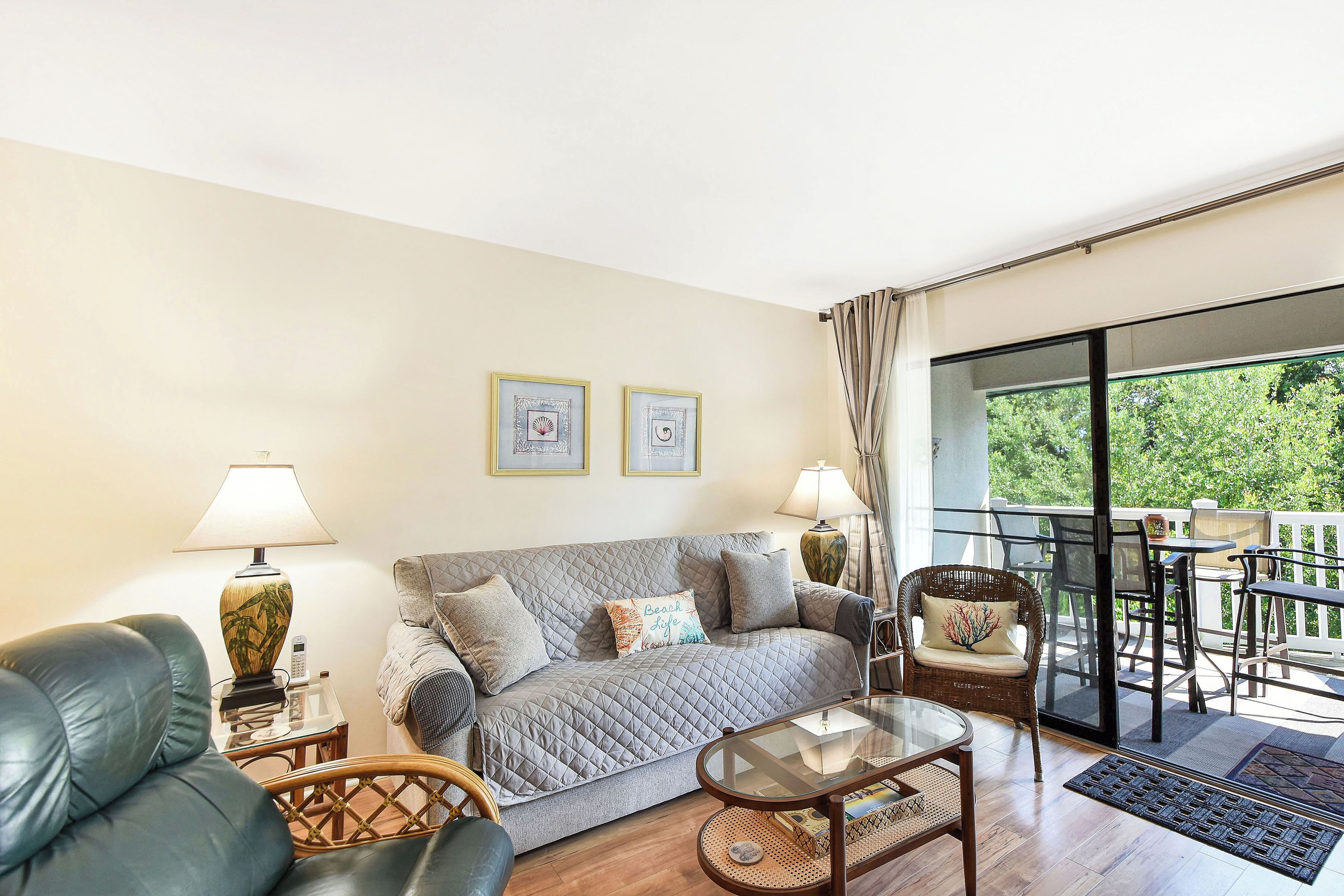 A living room with a sofa, two armchairs, a coffee table, and a balcony with outdoor furniture.