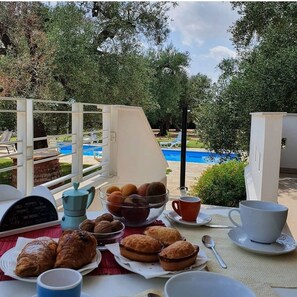 A breakfast setup with pastries, a coffee pot, and a bowl of fruits on a balcony overlooking a swimming pool. - Salento - Villa con piscina a pochi km dal mare e da Lecce (Leverano province of Lecce)