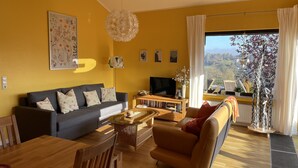 A living room with a sofa, a coffee table, and a TV. There is a window with a view of the outdoors. - Dream house on the Maar (Schalkenmehren)