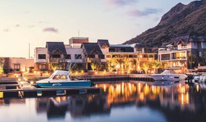 A marina with boats docked, a building with multiple balconies, and a mountainous backdrop. - Immaculate Two Beds Luxury Marina Apartment (Black River)