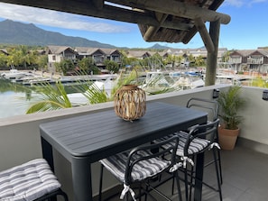 A balcony with a table and chairs, overlooking a marina with boats and houses in the background. - Immaculate Two Beds Luxury Marina Apartment (Black River)
