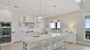Une cuisine moderne avec des meubles blancs, des appareils en acier inoxydable et un îlot central doté de tabourets de bar.