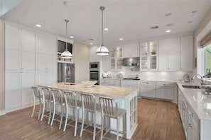 A modern kitchen with white cabinetry, a central island with bar stools, pendant lighting, and built-in appliances.