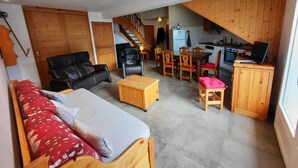 Ett kompakt bostadsutrymme med en soffa, ett matbord med stolar, en köksdel och en trappa som leder upp till en övre våning.