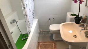 Un baño con bañera, inodoro, lavamanos y un tapete verde en el suelo.