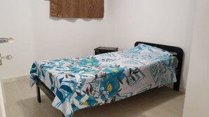 Una cama individual con una colcha estampada, una mesita de noche pequeña y una cortina colgada en la pared.