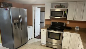 Eine kleine Küche mit Kühlschrank, Mikrowelle, Backofen und weißen Schränken.