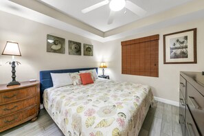 A bedroom with a bed, a dresser, a nightstand, a lamp, a ceiling fan, and wall art.