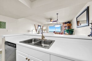A modern kitchen with a double sink, a ceiling fan, and a view of the ocean.