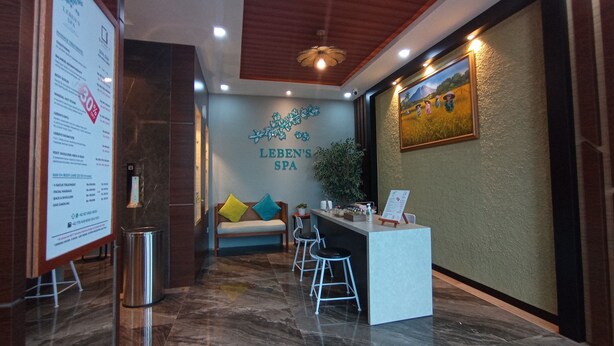 A reception area with a reception desk, a sofa with colorful cushions, a potted plant, and a wall-mounted sign for Lebens Spa. - Batam 1 Hotel (Batam)