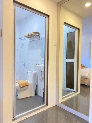 A modern bathroom with a toilet, sink, and shower area, visible through a glass door. - Batam 1 Hotel (Batam)