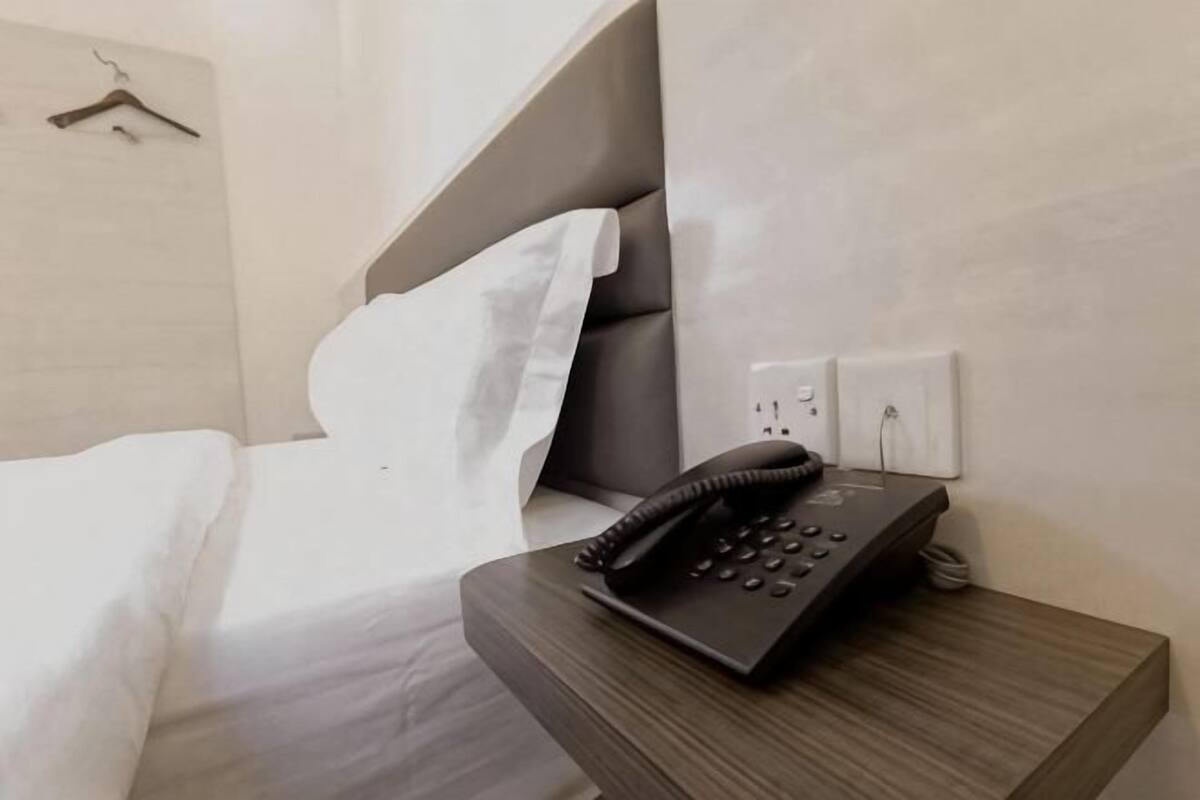 A hotel room with a bed, a bedside telephone, and a power outlet on the wall.