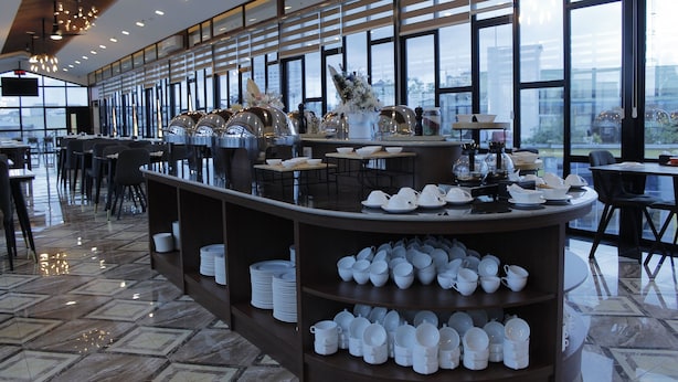 A modern restaurant with a central buffet area, large windows, and a polished tile floor. - Batam 1 Hotel (Batam)