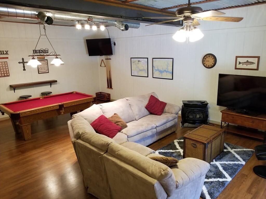Una sala de estar con mesa de billar, sofá, televisor y ventilador de techo.