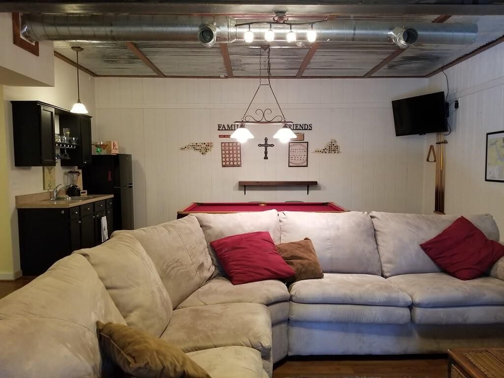 Ein Wohnzimmer mit einem beigefarbenen Ecksofa, einem Billardtisch und einer Decke mit freiliegenden Lüftungsrohren.