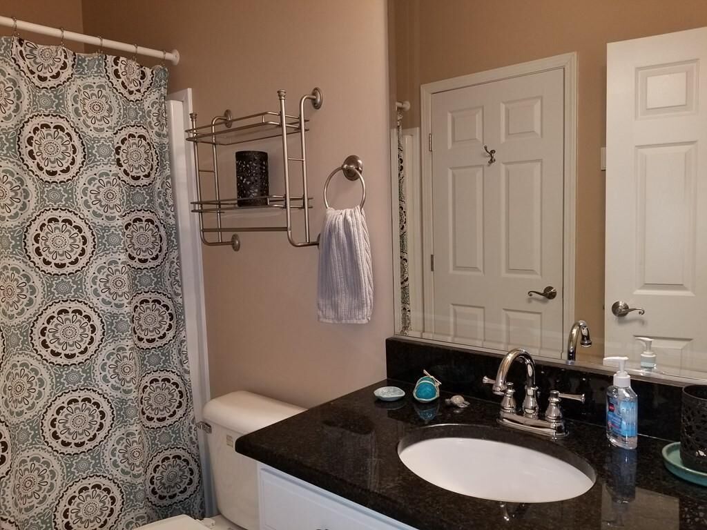 Een badkamer met een wit toilet, een zwart wastafel, een spiegel en een douchegordijn met een bloemenprint.