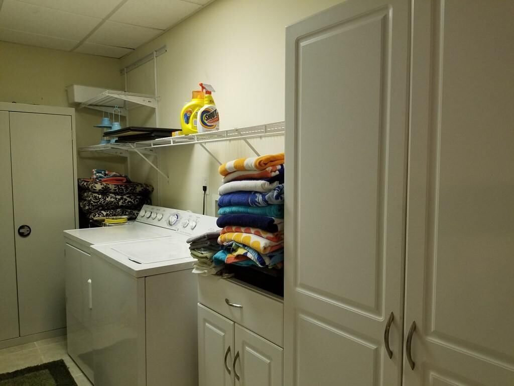 A laundry area with a washing machine, shelves with folded clothes, and a bottle of detergent.