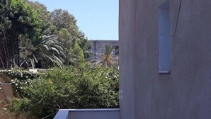 A rooftop terrace with a tiled floor, surrounded by vegetation and a building wall.