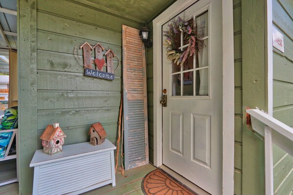 A green wooden door with a 'Welcome' sign, a birdhouse, and a wreath.