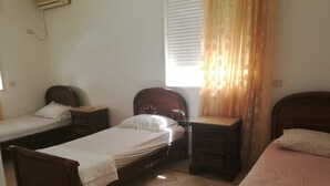 Una habitación con dos camas individuales, una mesita de noche con lámpara, una ventana con persianas y un aire acondicionado instalado en la pared.