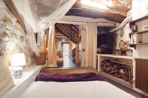 Una camera rustica con un letto, una lampada, un camino e una scala che conduce a un'altra stanza.