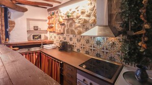 Una cuina rústica amb parets de pedra vista, bigues de fusta i un rebedor de rajola.