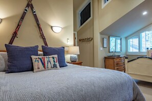 Een slaapkamer met een bed, nachtkastje, lamp, dressoir en raam.