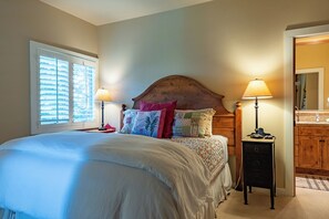 A bedroom with a large bed, two bedside lamps, a wooden headboard, and a window with blinds.