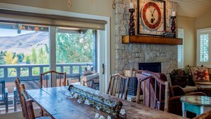 A dining area with a long wooden table, chairs, and a stone fireplace with a clock.