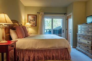 A hotel room with a bed, a dresser, a lamp, a poster, and a view through a door. - Wildflower Condo 671 - Beautiful Sun Valley Resort Condo For 8 Guests (Sun Valley)