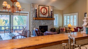 A spacious living area with a stone fireplace, a wooden bar, and a large window overlooking a scenic landscape.